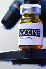 Vial of Covid-19 vaccine next to a microscope