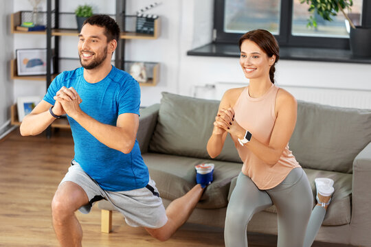 sport, fitness, lifestyle and people concept - smiling man and woman exercising and doing squats in low lunge at home