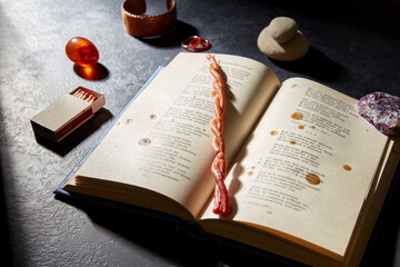 occult science and supernatural concept - magic book, wax candle, matches and gem stones for ritual