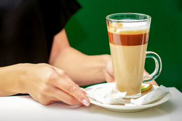 Close up of female waiter gives cup of coffee latte with candy in plate on the table
