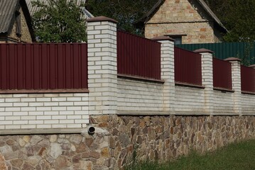 fence wall of white bricks and red metal on a brown stone foundation outside in green grass