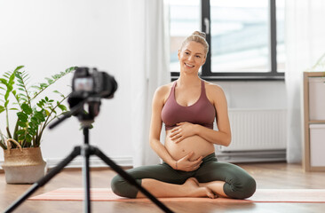 Fototapeta na wymiar sport and people concept - happy pregnant woman or blogger with camera on tripod recording online yoga class at home