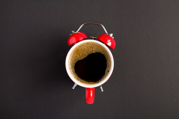 Top view of coffee on the dial of the red alarm clock in the center of the dark background