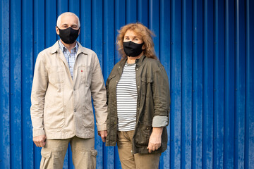Senior couple wearing mask to protect from viruses on blue background, copyspace