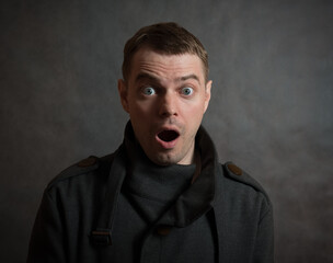 Man in coat on dark background with surprised face.