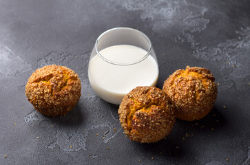 Delicious homemade pumpkin muffins with spicy sugar crust with milk on black textured background	