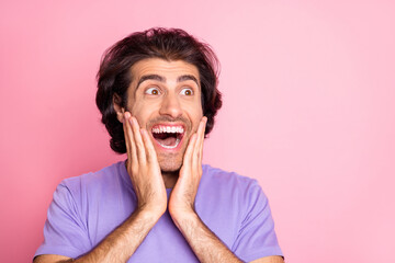 Photo of amazed man hands cheeks look empty space wear violet t-shirt isolated pastel pink color background