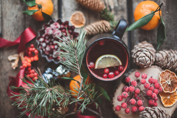 Fototapeta na wymiar cup of hot tea with lemon, cranberry. decorated with fir tree branches, tangerine, cones and berryes on wooden background. top view. winter christmas hot drink