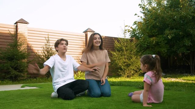 Three children of different ages on a summer day, sitting on the grass, play a game, explaining something to each other and emotionally gesturing. Positive and friendship.