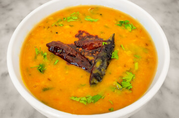 Indian Dish Lentils (Dal) Curry in a white bowl garnished with dry chillies and coriander leaves