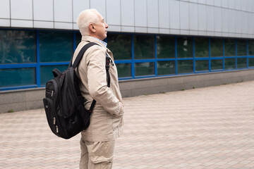 Senior man wearing backpack outdoors in city landscape near office buildings
