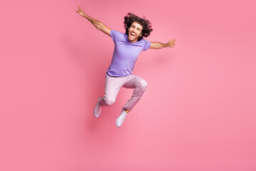 Full size photo of positive bristled happy young man make hands plane wings jump fly wear pink...