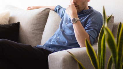 Primer plano a un hombre blanco adulto sentado sobre un sofá gris en una blanca y brillante habitación pensando y preocupado durante una jornada de trabajo en la oficina
