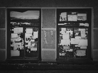 Black and white moody street photography, scratched advertising on old windows. Torn urban posters on a building facade, different crumpled billboard paper and stickers. Grunge texture, dirty walls.