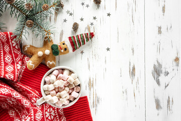 New Year background. A cup of cocoa with marshmallows, gingerbread, a branch of a Christmas tree with cones, a red sweater on a white wooden background with copy space. Flat layout
