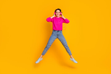 Fototapeta na wymiar Photo of attractive lady jump high up good mood listen earphones wear pink pullover jeans shoes isolated yellow color background