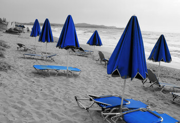 Beach umbrellas and chairs on greek sandy beach. Blue and grey colors landscape  