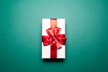Close-up of white gift box with red bow, on green background.