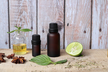 aromatic essential oil bottles , lemon, basil, anise, and extracted citrus oil are on the wooden table in the kitchen with background of wooden texture