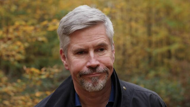 Portrait of a disappointed handsome middle aged man in nature, slow motion. Mature caucasian man sighs, shakes his head and closes his eyes in frustration. Attractive autumn forest background.