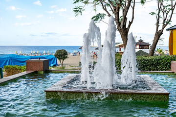 Turkey, Alanya - October 22, 2020: Fountain in a public park against the background of Cleopatra beach in Alanya. Pool with vertical jet of water on the Mediterranean coast