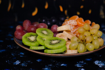 Fruits, grapes, tangerines, bananas, kiwi in a blue porcelain plate. black wooden floor, fruit plate