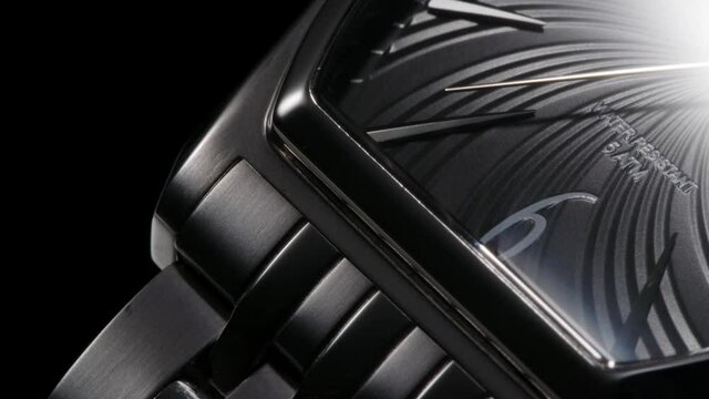 Closeup view of rotating luxury swiss watch with metallic bracelet and ribbed black clock face 