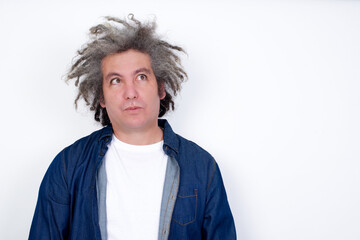 Handsome middle aged Caucasian man with afro gray hair, against white wall, , looks pensively aside, plans actions after university, imagines what to do Thinks over about new project.
