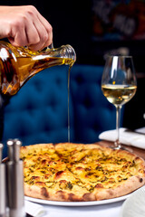 Hand with a bottle of oil pours pizza.