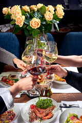 Four hands with glasses of wine over a table with food.