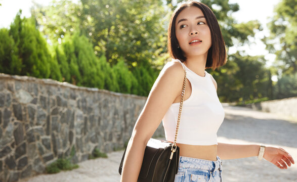 Summer sunny lifestyle fashion portrait of young stylish hipster Asia woman walking on the street, wearing cute trendy outfit, turn behind and looking thoughtful