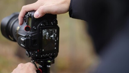 Photographer adjusting settings of a professional DSLR camera. Slow motion. Using a tripod or camera stand while changing aperture and shutter speed. Outdoors in nature. - Powered by Adobe