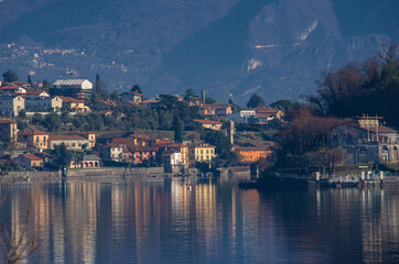 Fototapeta na wymiar Reflections on the calm water of the lake of winter colors of sunny villages.Como lake, lombardy, Italy