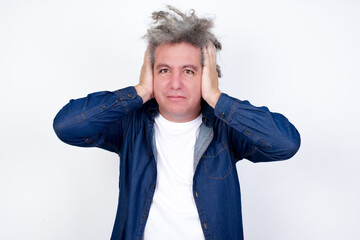 Frustrated Handsome middle aged Caucasian man with afro gray hair, against white wall,  plugging ears with hands does not wanting to listen hard rock, noise or loud music.