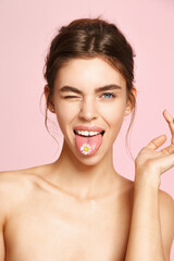 Beauty and skin care. Naked woman holding chammomile on tongue and winking, clean face without...