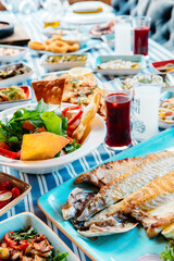 Fototapeta na wymiar Grilled fish, salads and vegetables. Seafoods, grilled meat, meze, raki, ouzo, appetizers and salads on the table in Greek or Turkish Fish Restaurant for dinner or lunch at the beach.