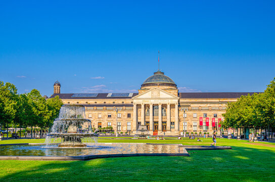 Wiesbaden, Germany, August 24, 2019: Kurhaus or cure house spa and casino building and Bowling Green park with grass lawn, trees alley and pond with fountain in historical city centre, State of Hesse