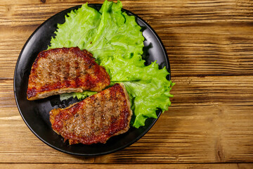 Grilled pork steaks with lettuce leaves on wooden table. Top view