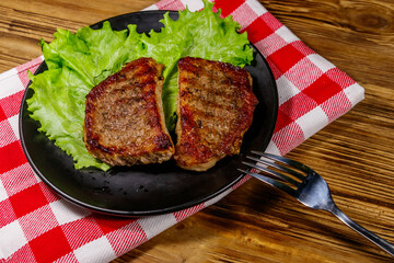 Grilled pork steaks with lettuce leaves on wooden table