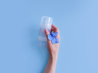 Mockup of transparent bottle of intimate lubricant gel, female hand and blue flowers on blue...