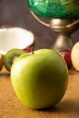 Green apple in the foreground on rustic wood and fruits in the background, selective focus.