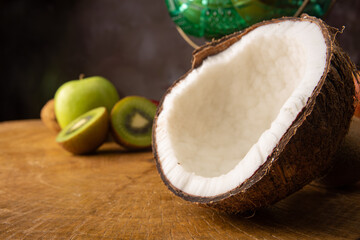 Coconut in the foreground on rustic wood and fruits in the background, selective focus.
