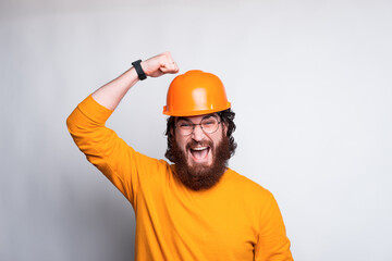 Portrait of funny young bearded architect hitting on helmet, safety first.