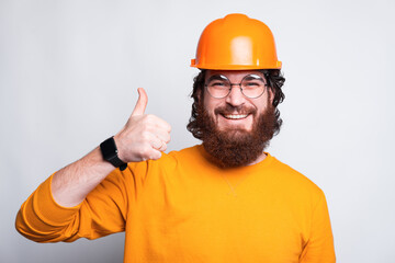 Portrait of smiling young architect showing thumb up and wearing helmet.
