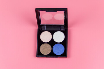 Set of four round eye shadow in a plastic black box on a pastel pink background. Flat lay