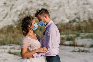 Young loving couple in medical masks in park during quarantine on wedding day.