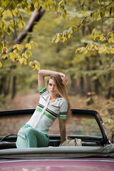 stylish woman with hand above head looking at camera while posing in cabriolet