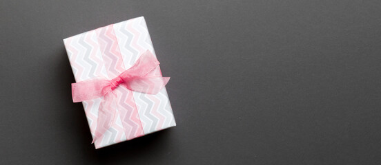 wrapped Christmas or other holiday handmade present in paper with pink ribbon on black background. Present box, decoration of gift on colored table, top view with copy space