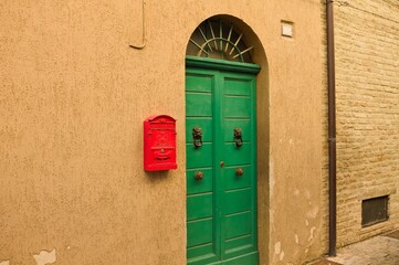 Red mailbox hanging on the wall of a house with a green door (