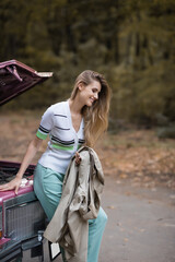 smiling woman holding cape while standing near broken vintage car on road